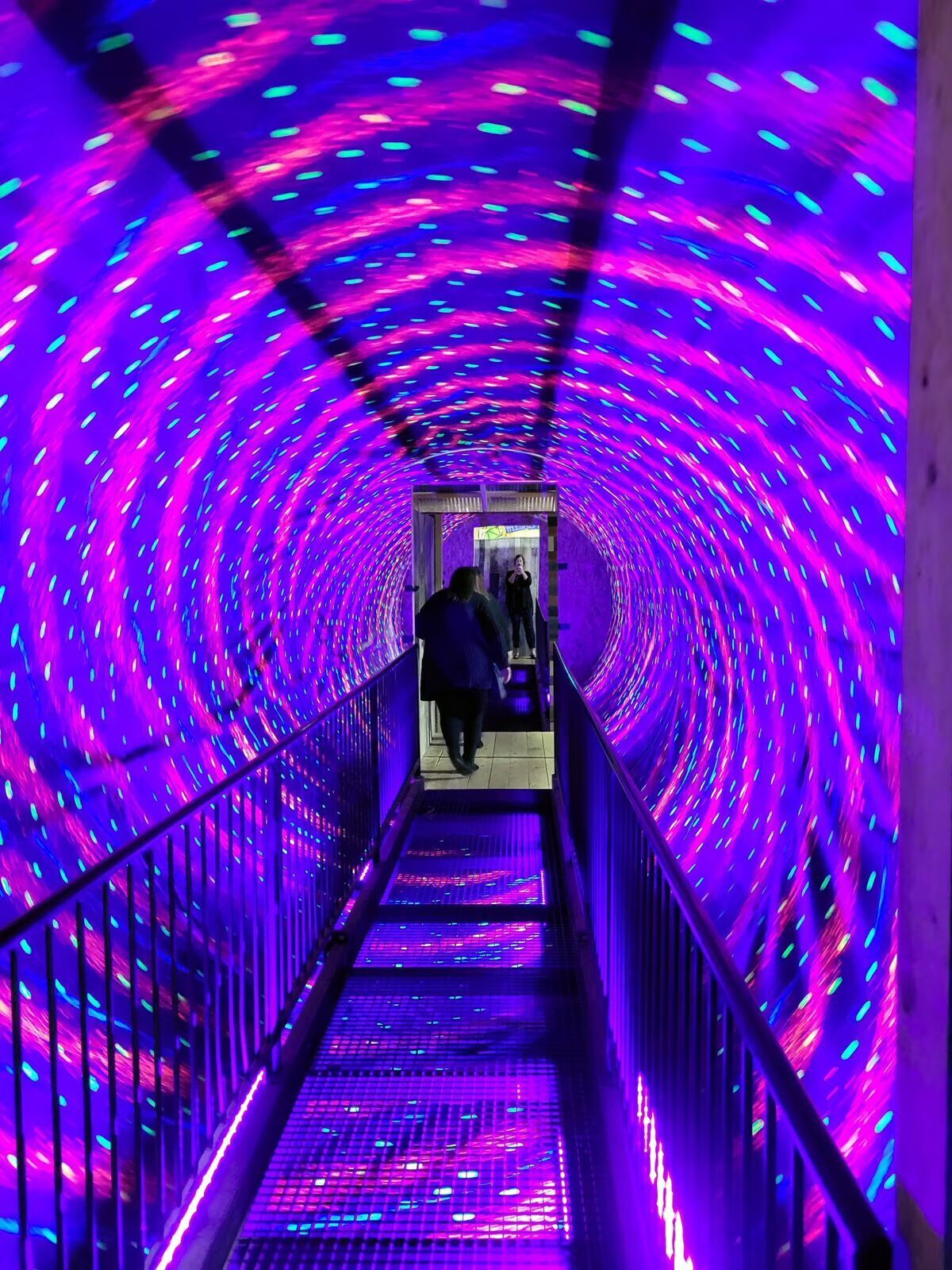 A person walking through a brightly lit, swirling purple tunnel.