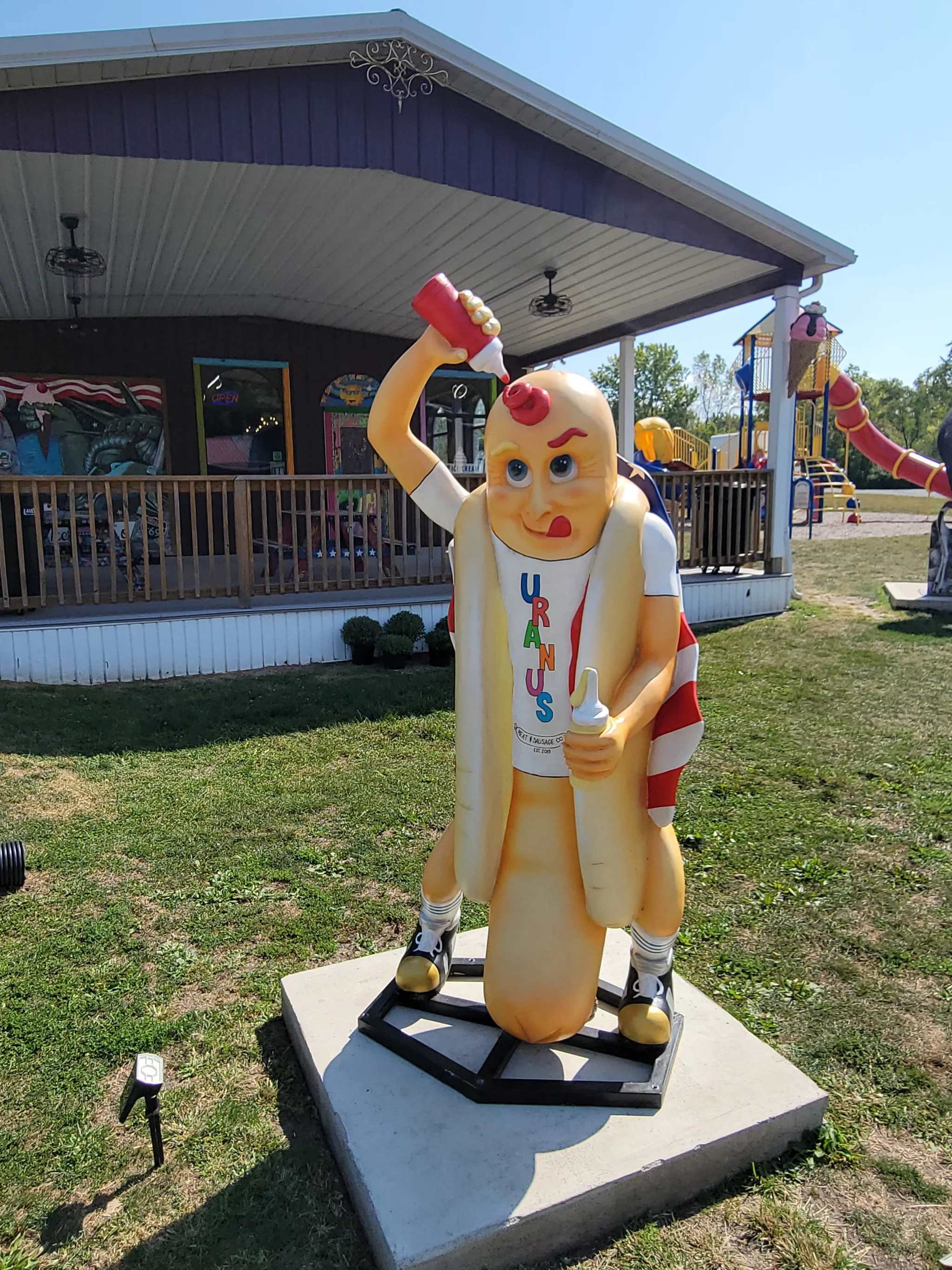 A colorful statue of a cartoonish hot dog character holding a drink.