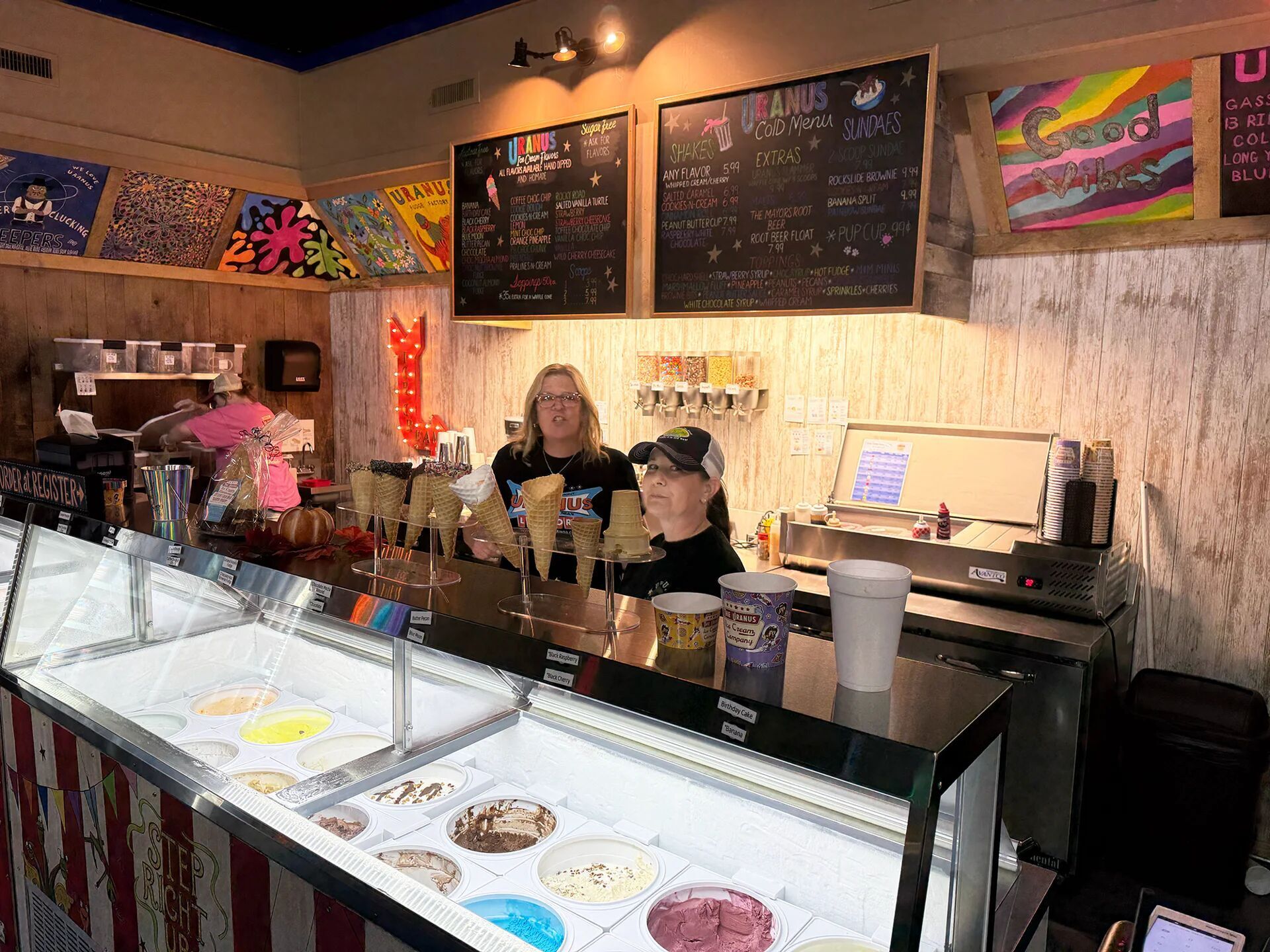 Ice cream shop counter with staff and colorful menu in the background.