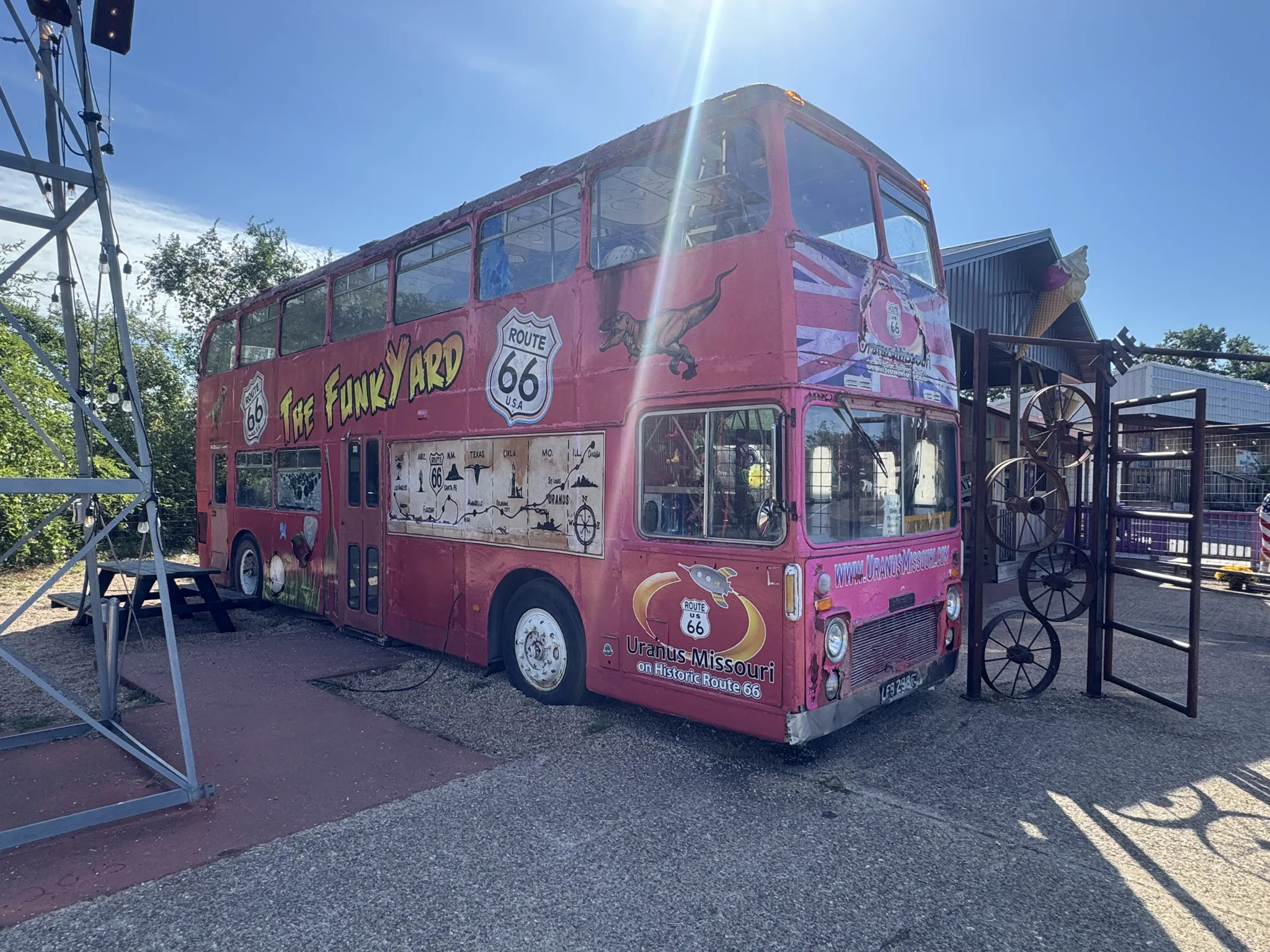 Red double-decker bus parked outdoors in bright sunlight at Uranus Fudge Factory and General Store in Uranus, Missouri.