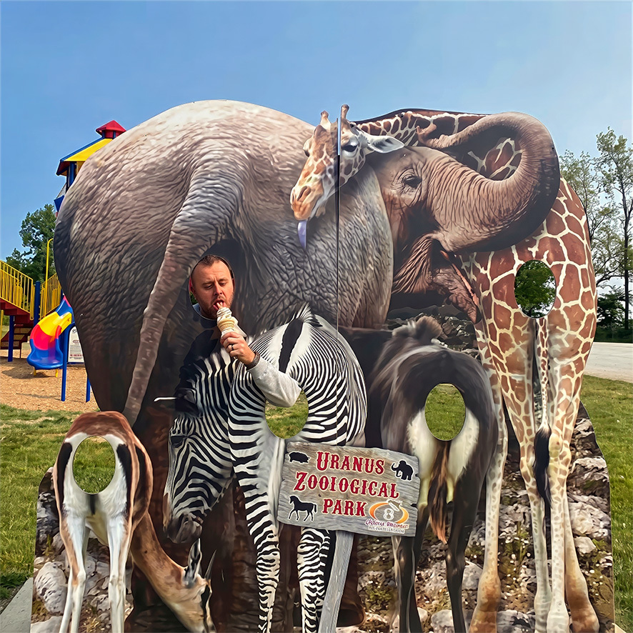 Man posing with giant safari animal statues at Uranus Zoological Park in Anderson, Indiana