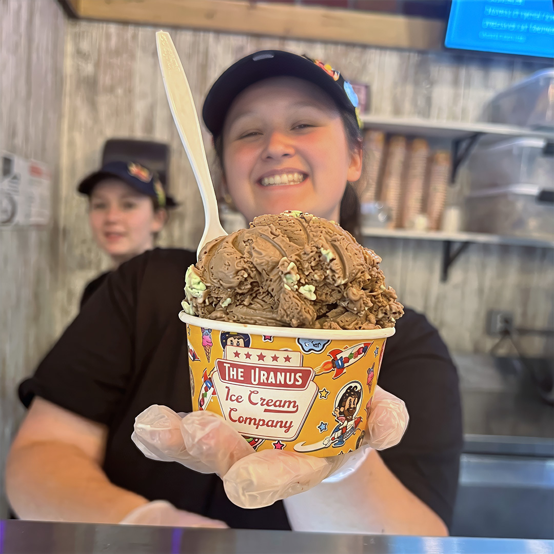 Employee holding a large cup of ice cream at the Uranus Ice Cream Co. counter in Anderson, Indiana