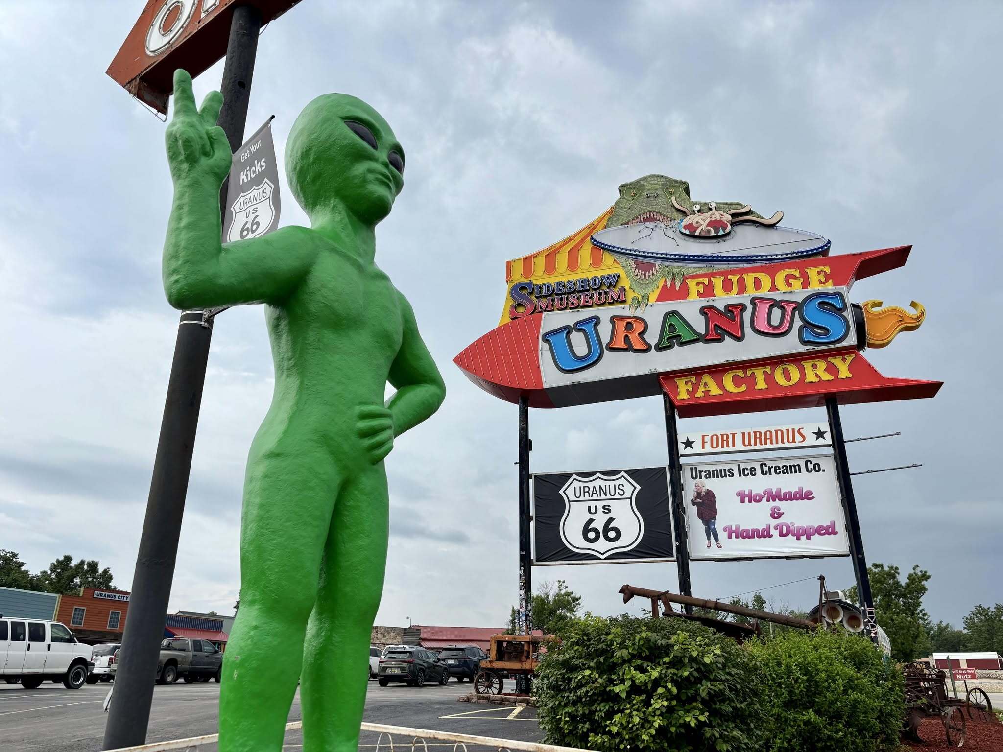 Giant green alien statue giving a peace sign in front of the Uranus Fudge Factory and Sideshow Museum sign on Route 66 in St. Robert Missouri