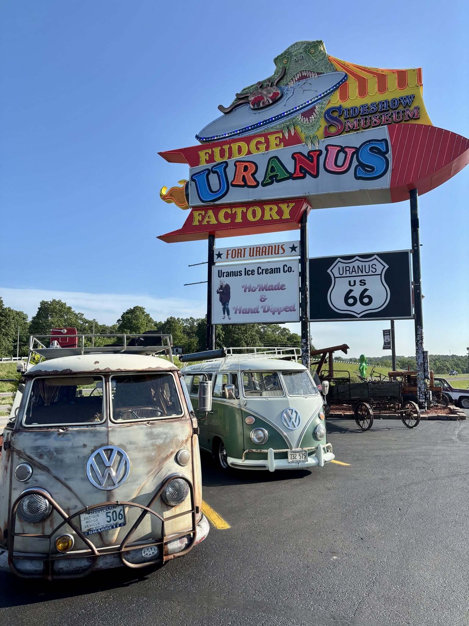 Two vintage Volkswagen buses parked beneath the Uranus Fudge Factory neon sign on historic Route 66 in Missouri
